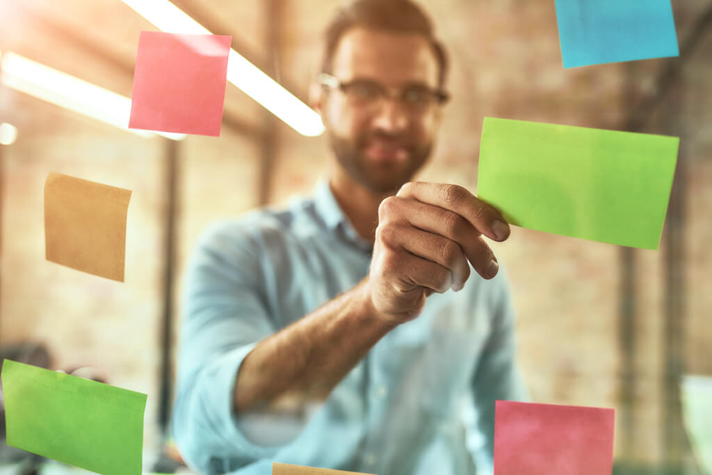 project manager putting sticky notes with tasks on a glass board