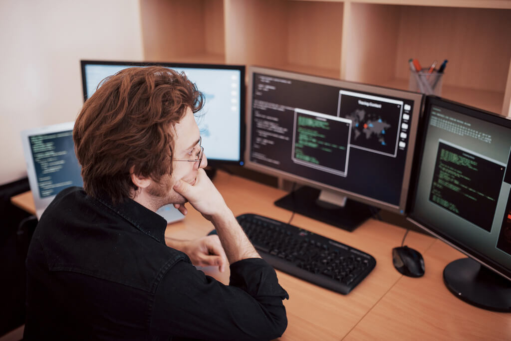 software developer working on his code with 3 monitors